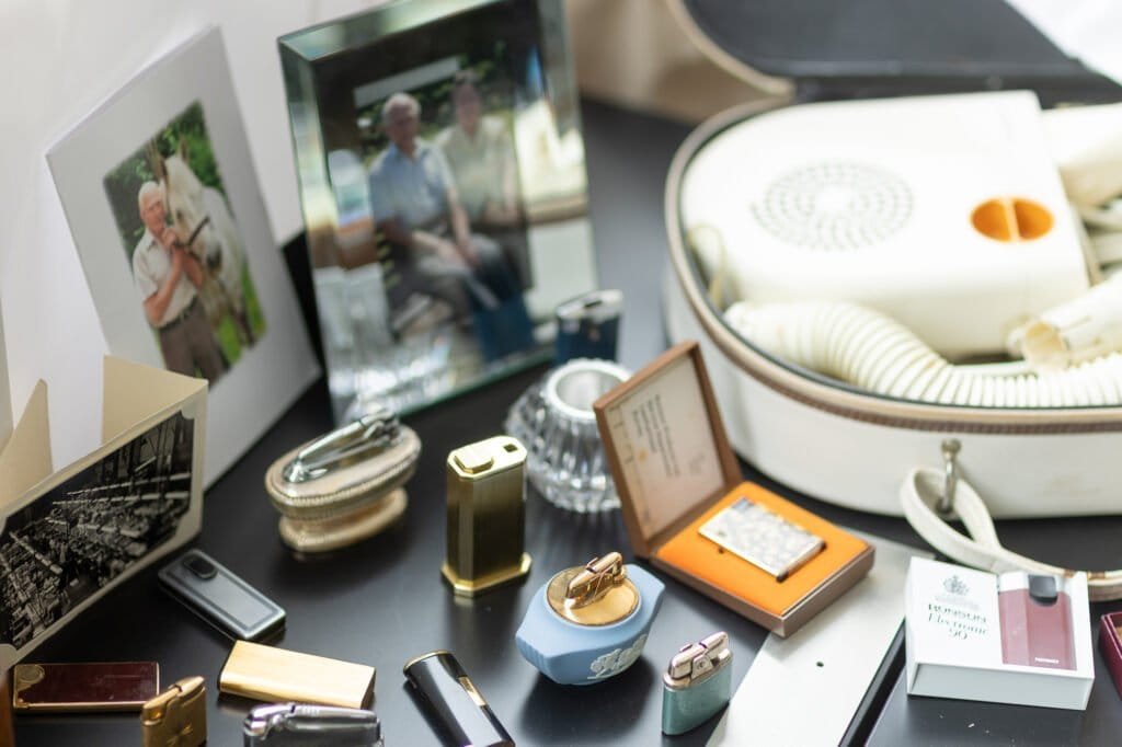 Ronson lighters, including a boxed Electronic 90 and a blue and gold table lighter, beside a white hairdryer and two framed photos.