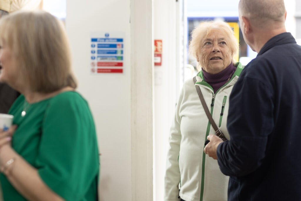 An attendee in a cream jacket looks up as a man in a navy jumper talks to her at the Ronson Reunited event in 2026.