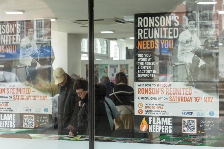 Flame Keepers poster in the window reading 'Ronson's Reunited needs you' and 'Saturday 16th May', with attendees reflected in the glass.