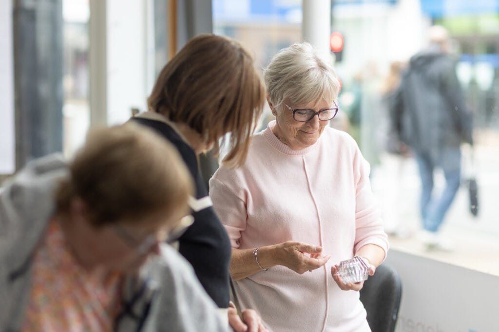 An attendee in a pink cardigan and glasses looks at a small clear object in her hands at the Ronson Reunited event in 2026.